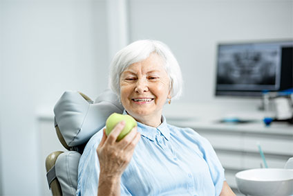 Seniorin mit gesundem Lächeln hält einen Apfel in der Hand